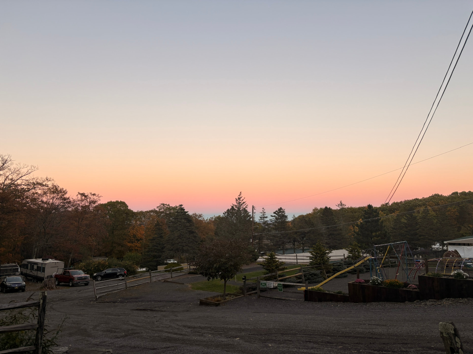 Pink and peach twilight sky over the campground playground, parked campers and a split-rail fence
